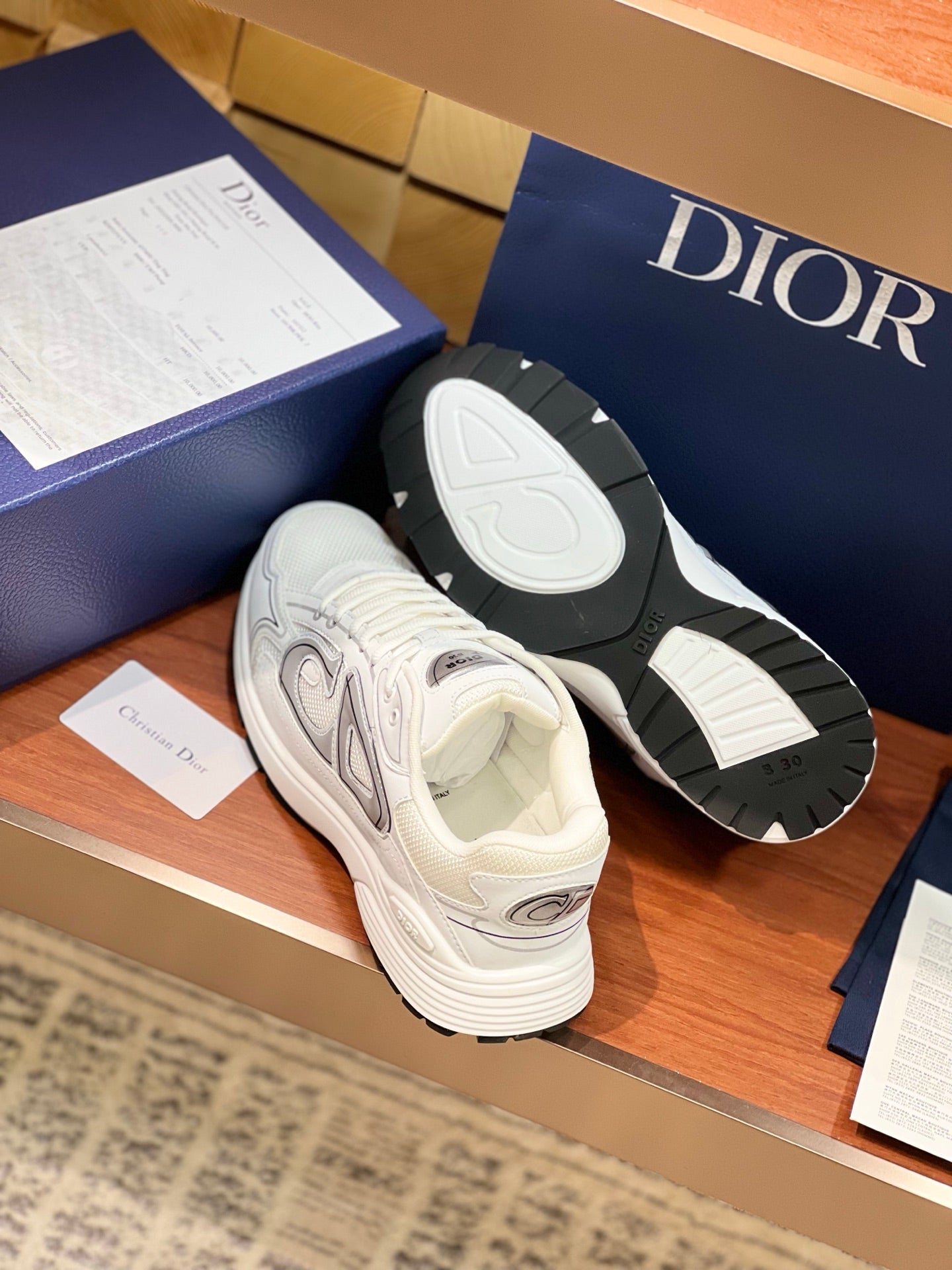 White Dior sneakers with textured black outsoles, lace-up uppers with gray emblems
