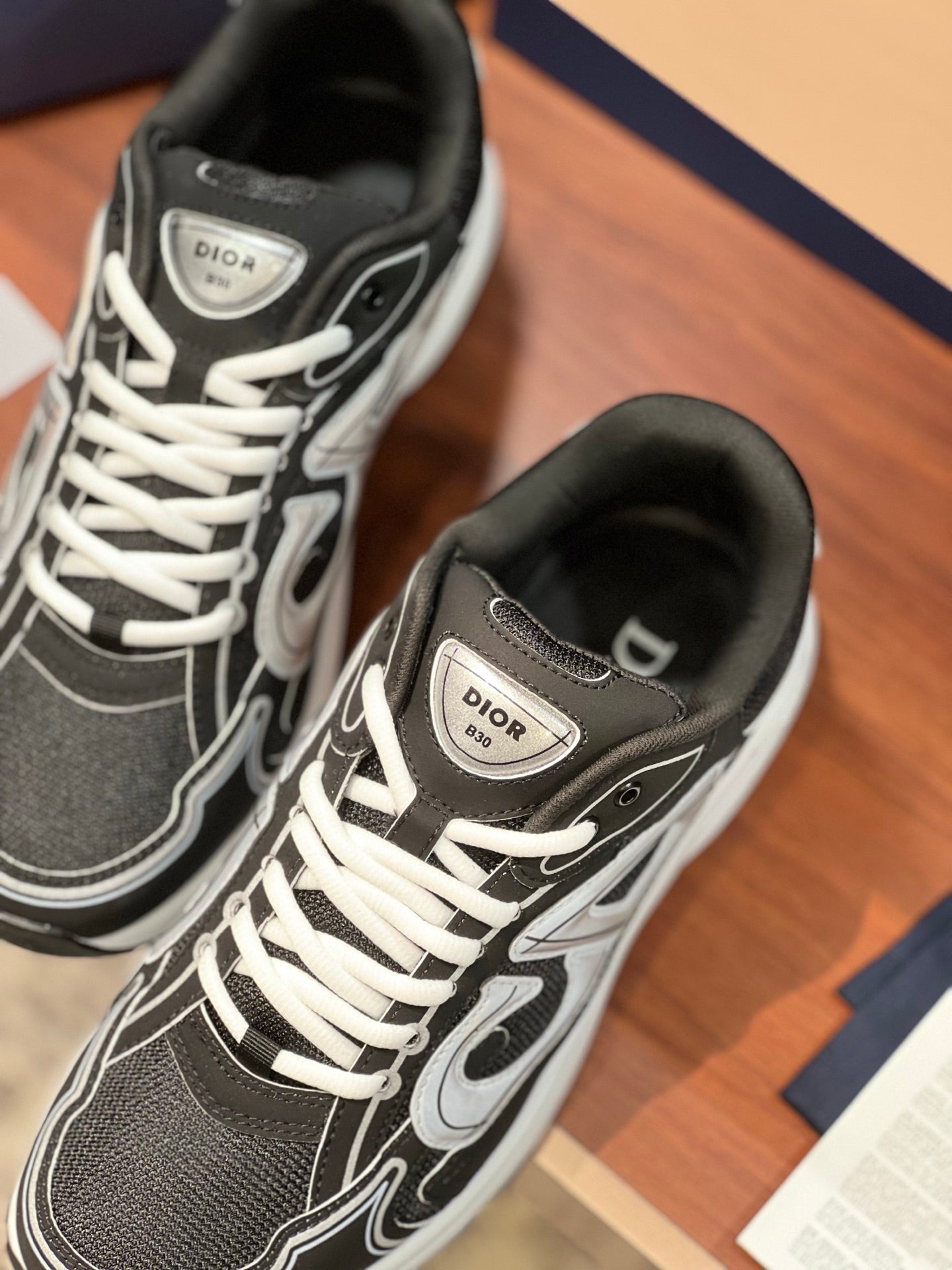 Dior ladies sneakers close-up, black upper with white lace pattern and emblem