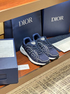 Navy Dior lace-up sneakers with white midsoles and swirl logo panels, angle view