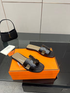 Black leather slide sandals on orange shoebox, wide strap and cream footbed