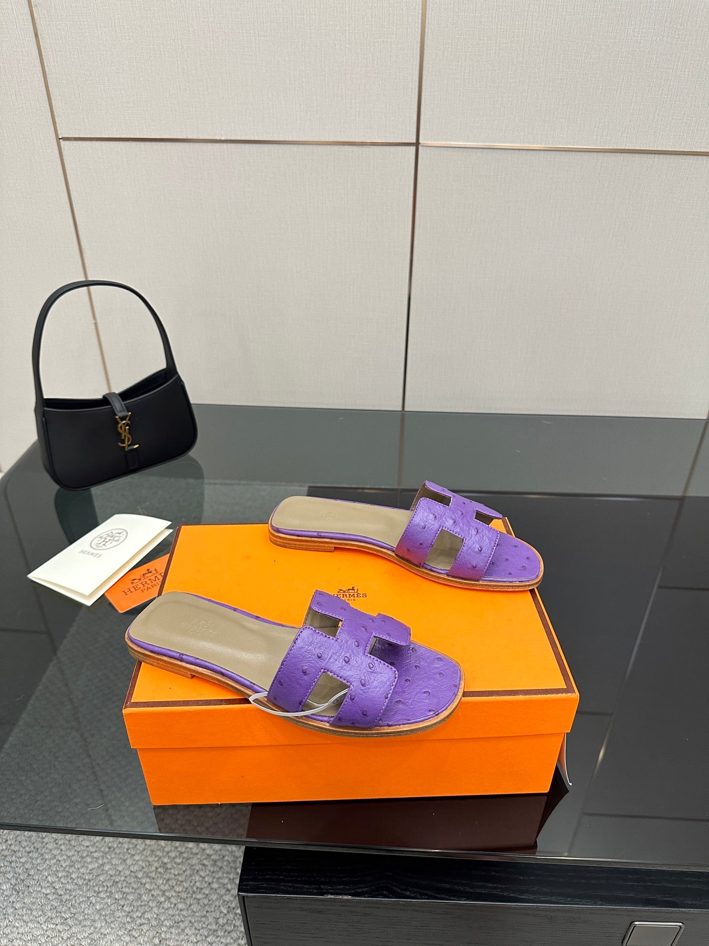 Hermes purple slide sandals with H-style cutout strap, angled view on orange box