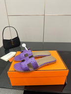 Hermes purple slide sandals with H-style strap detailing, side view on orange box