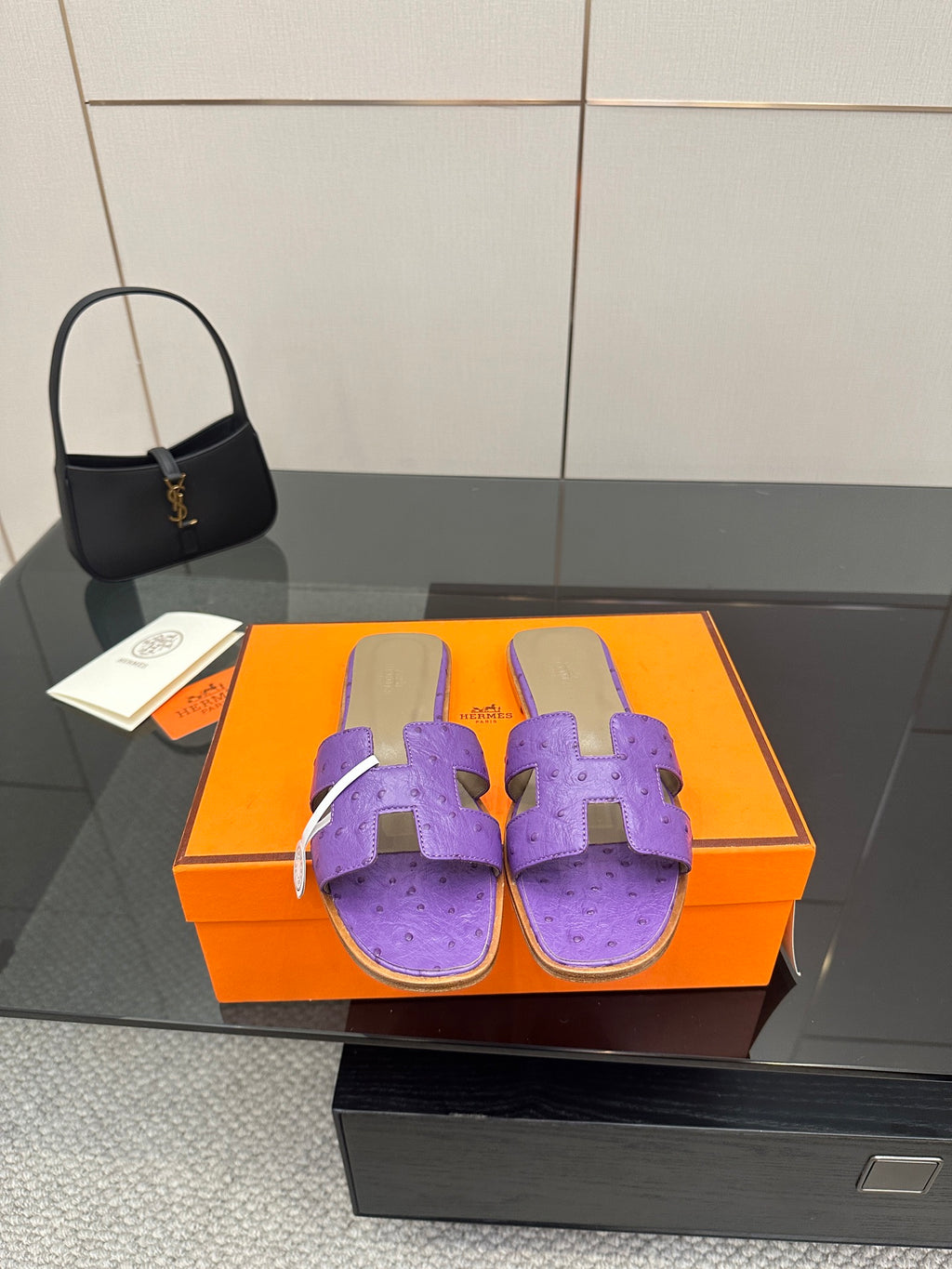 Hermes purple slide sandals with H-style cutout strap, shown on a display box