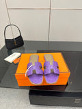 Hermes purple slide sandals with H-style cutout strap, shown on a display box