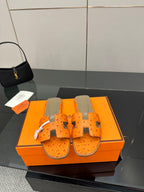 Orange leather slide sandals with cutout straps and metal buckle details