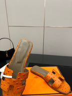 Orange leather slide sandals close-up with perforated texture and metal buckle strap