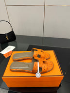 Orange leather slide sandals viewed from above with openwork cross straps and buckles