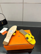Hermes yellow slide sandals with gray footbed and black H straps on orange box