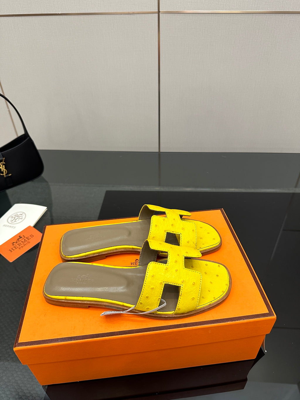 Hermes yellow slide sandals with black H straps, angled view and gray footbed