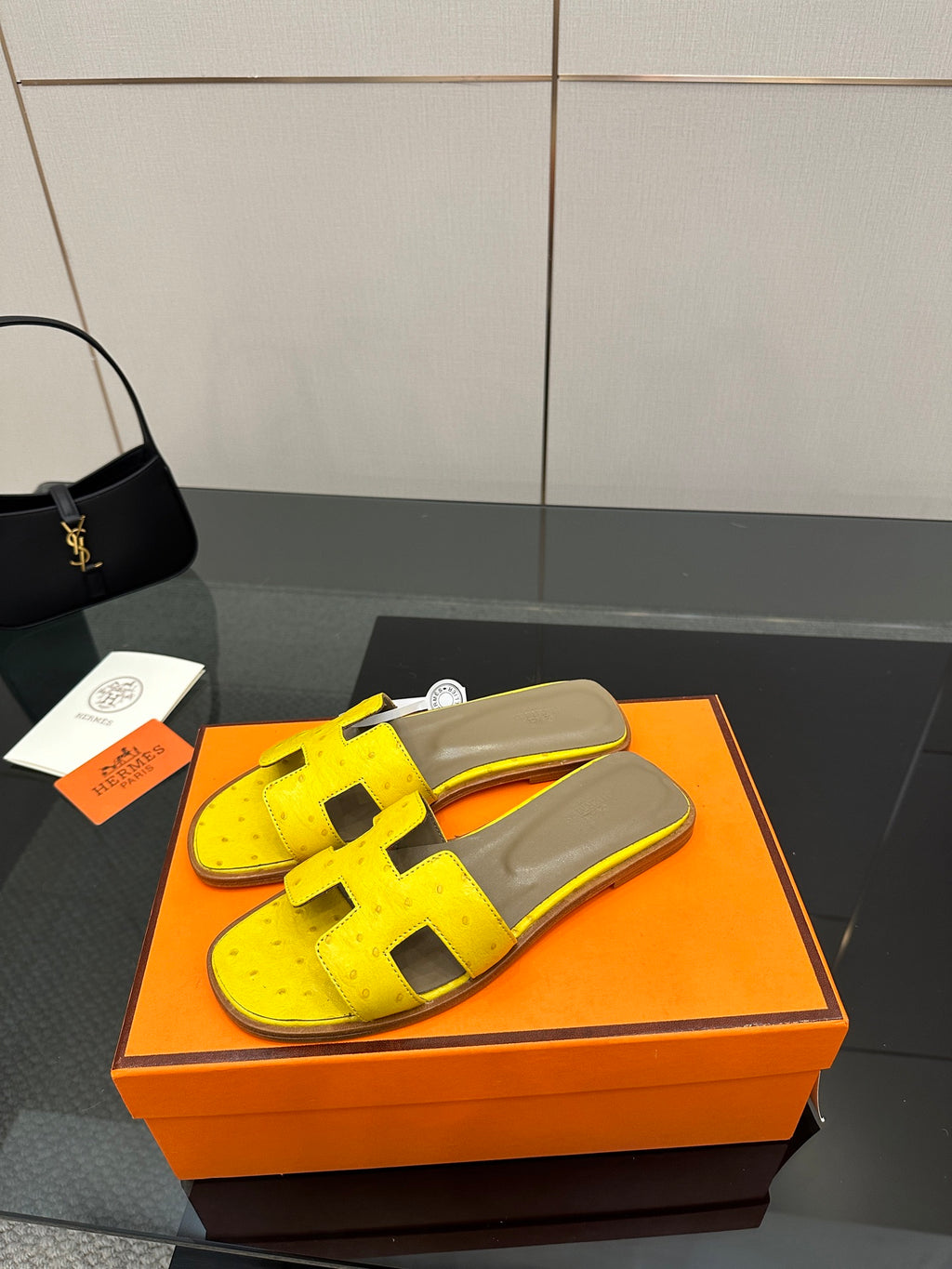 Hermes yellow slide sandals with black H straps and gray footbed in orange box