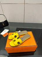 Hermes yellow slide sandals with black H straps and gray footbed in orange box
