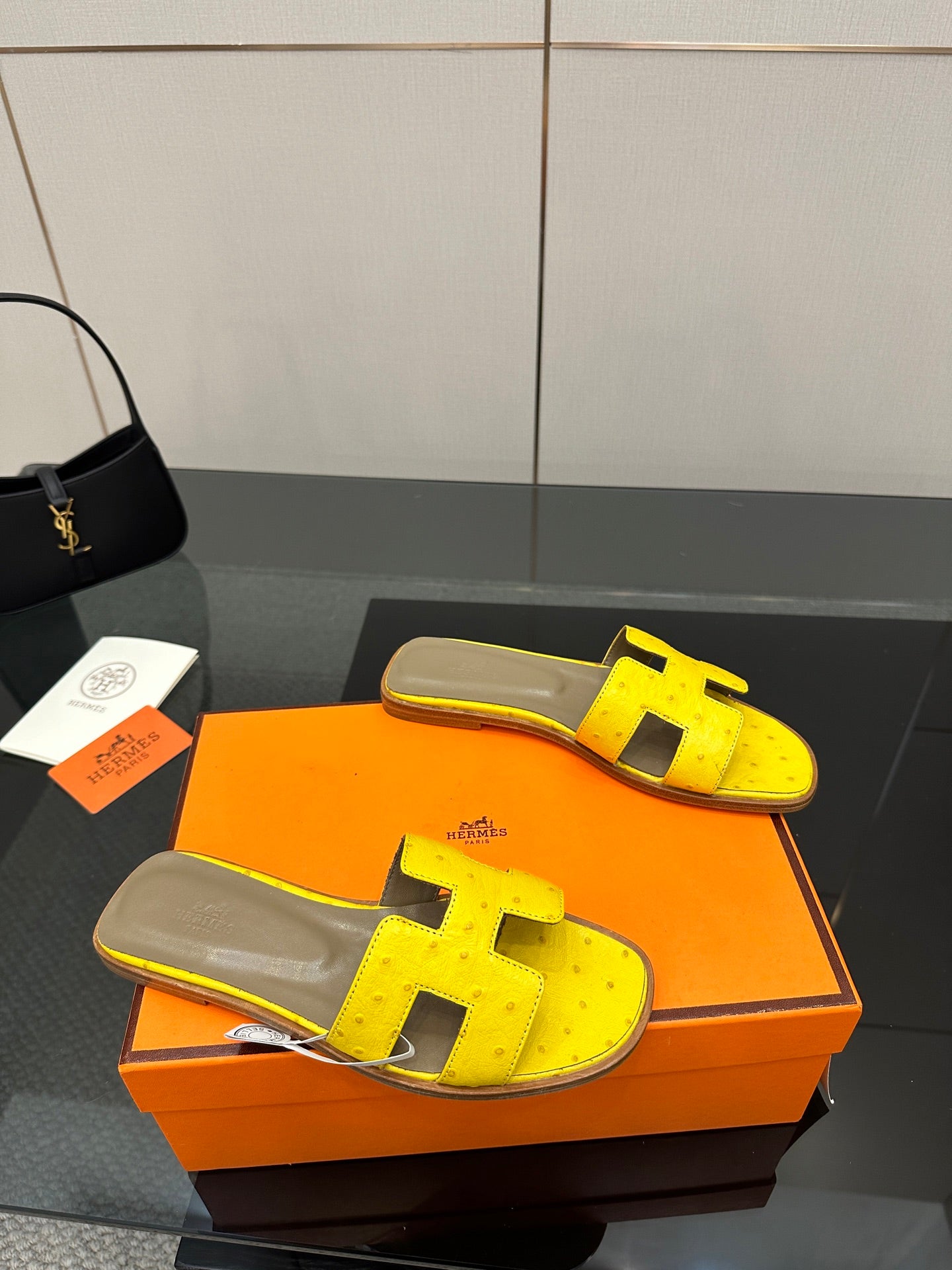 Hermes yellow slide sandals with black H straps and gray leather footbed, angled view