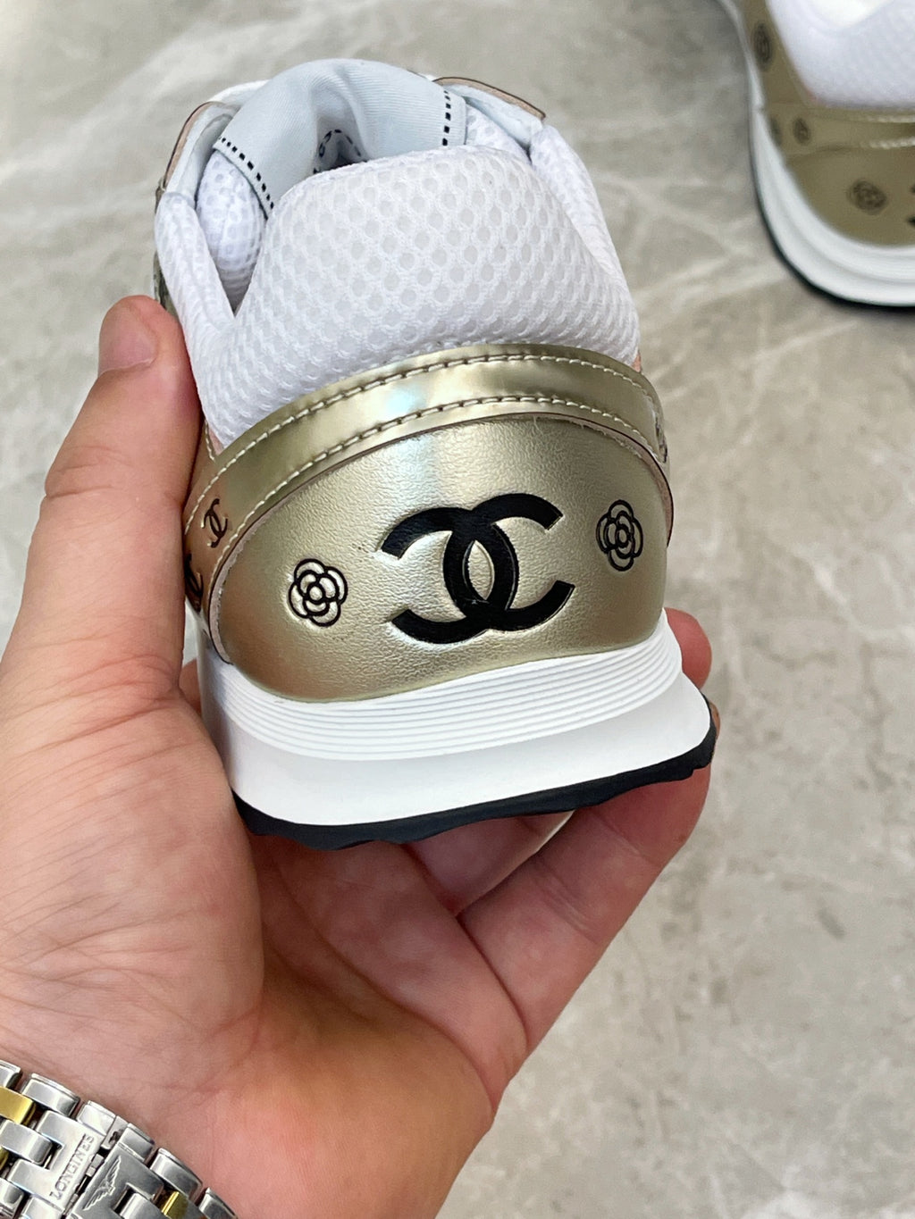 Unisex sneaker heel close-up, gold leather panel with black CC logo and white lining