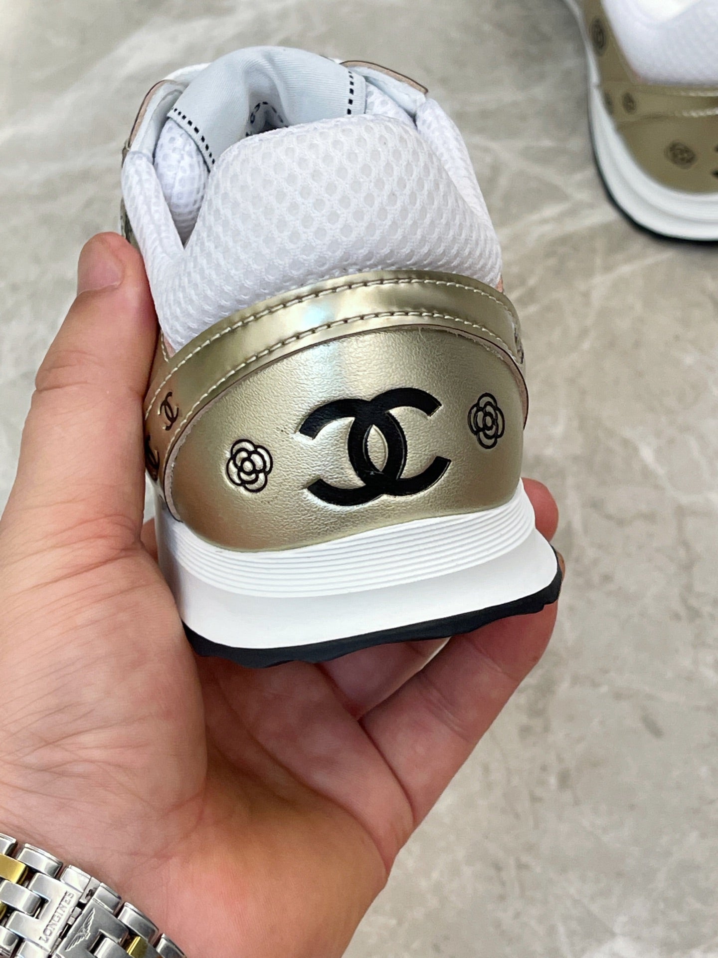 Unisex sneaker heel close-up, gold leather panel with black CC logo and white lining