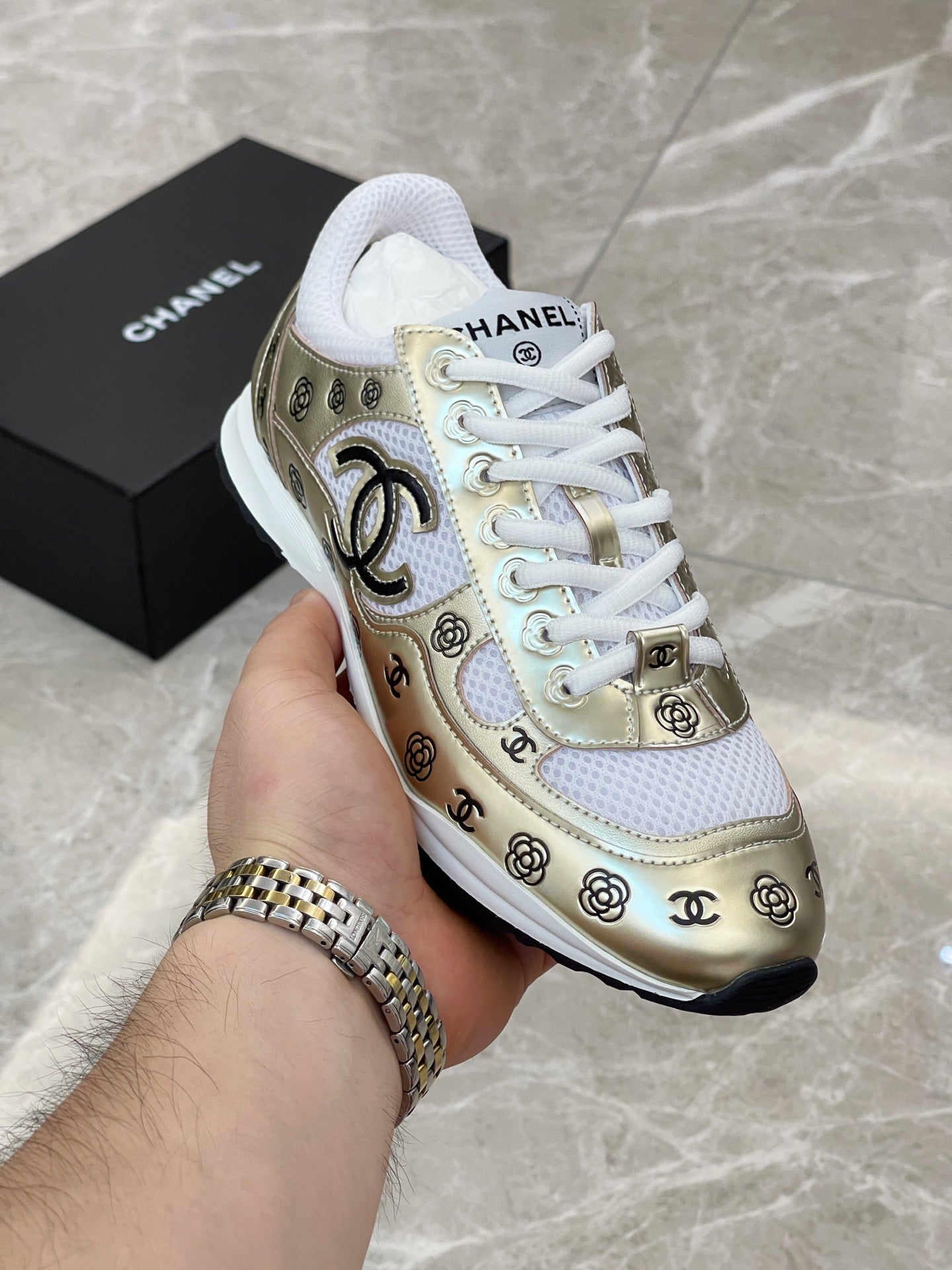 Unisex sneaker in hand, gold and white side panel with logo and white laces