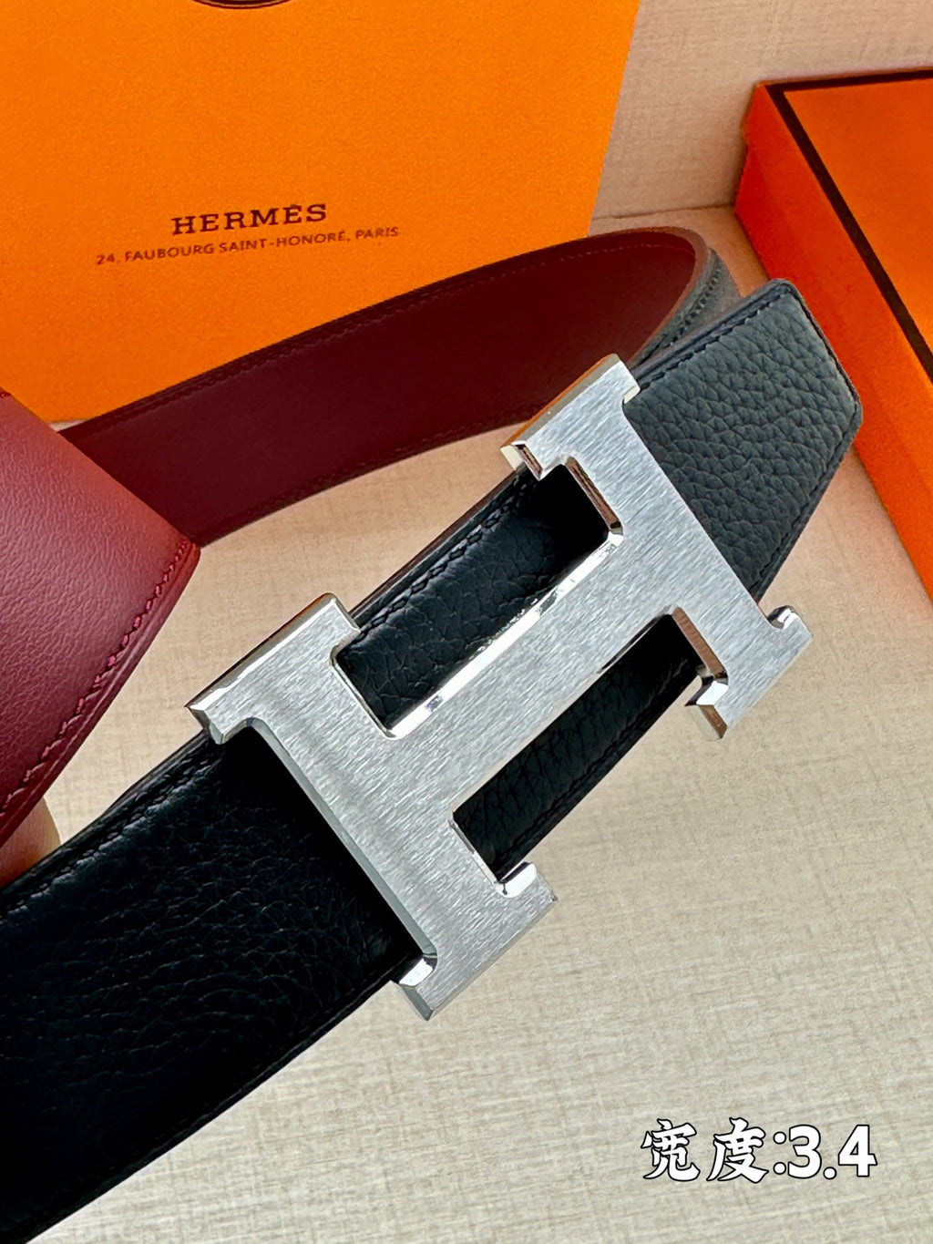 Navy leather belt close-up with silver H buckle and textured strap.