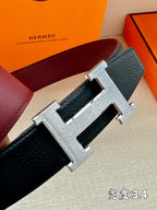 Navy leather belt close-up with silver H buckle and textured strap.