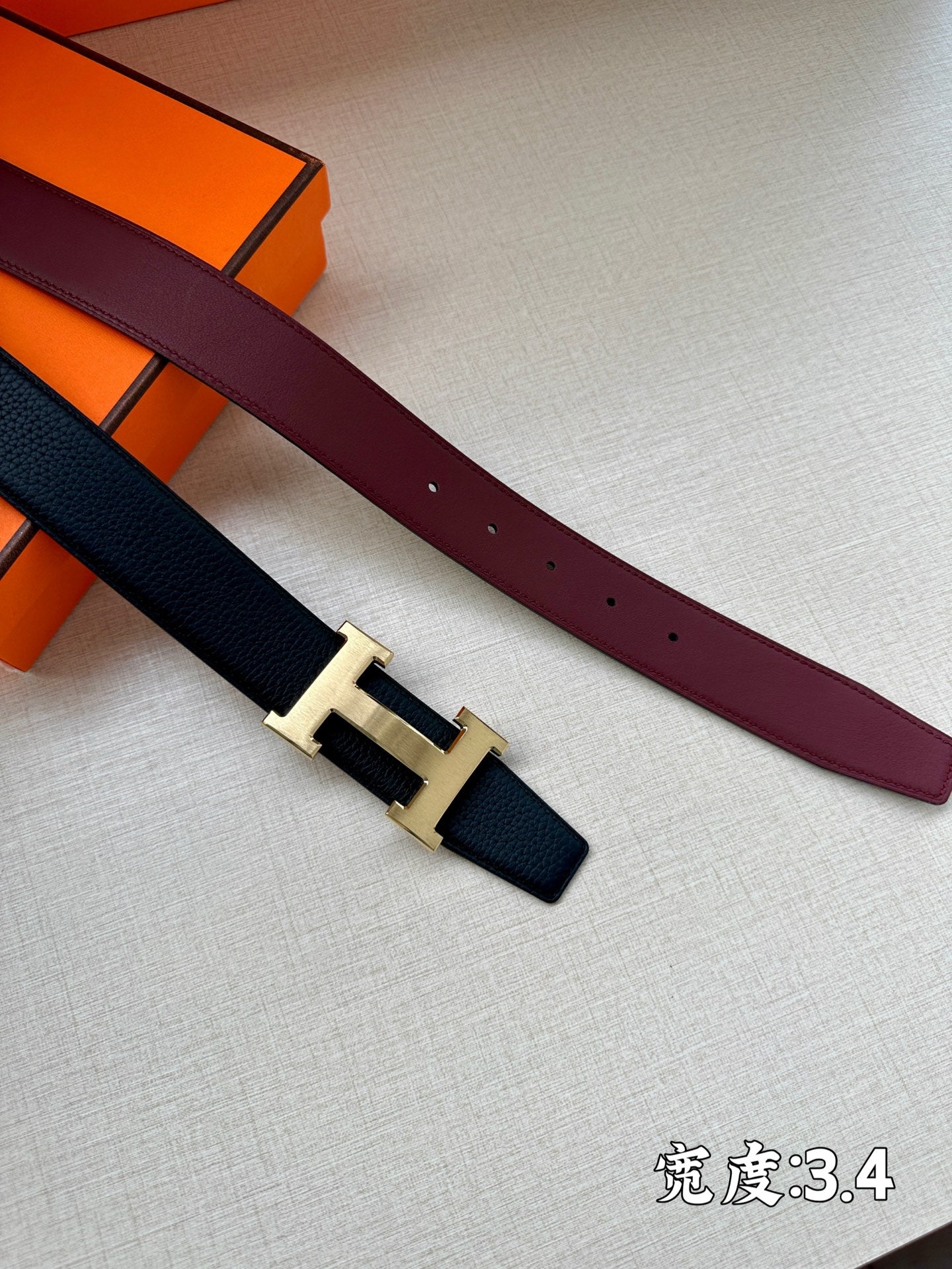 Dark navy and burgundy leather belts with silver H buckle in orange boxes.