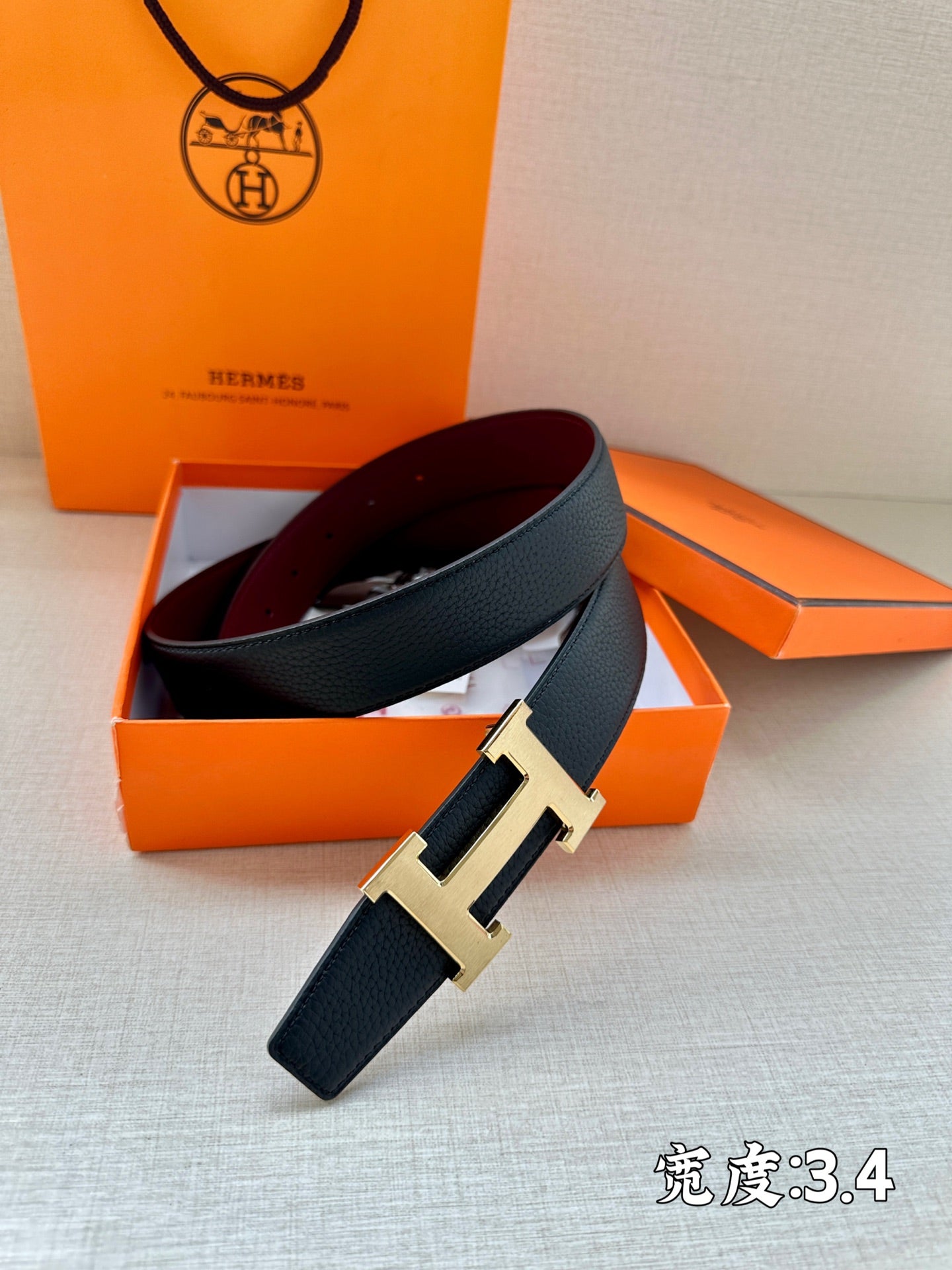 Navy leather belt with silver H buckle on orange boxes.