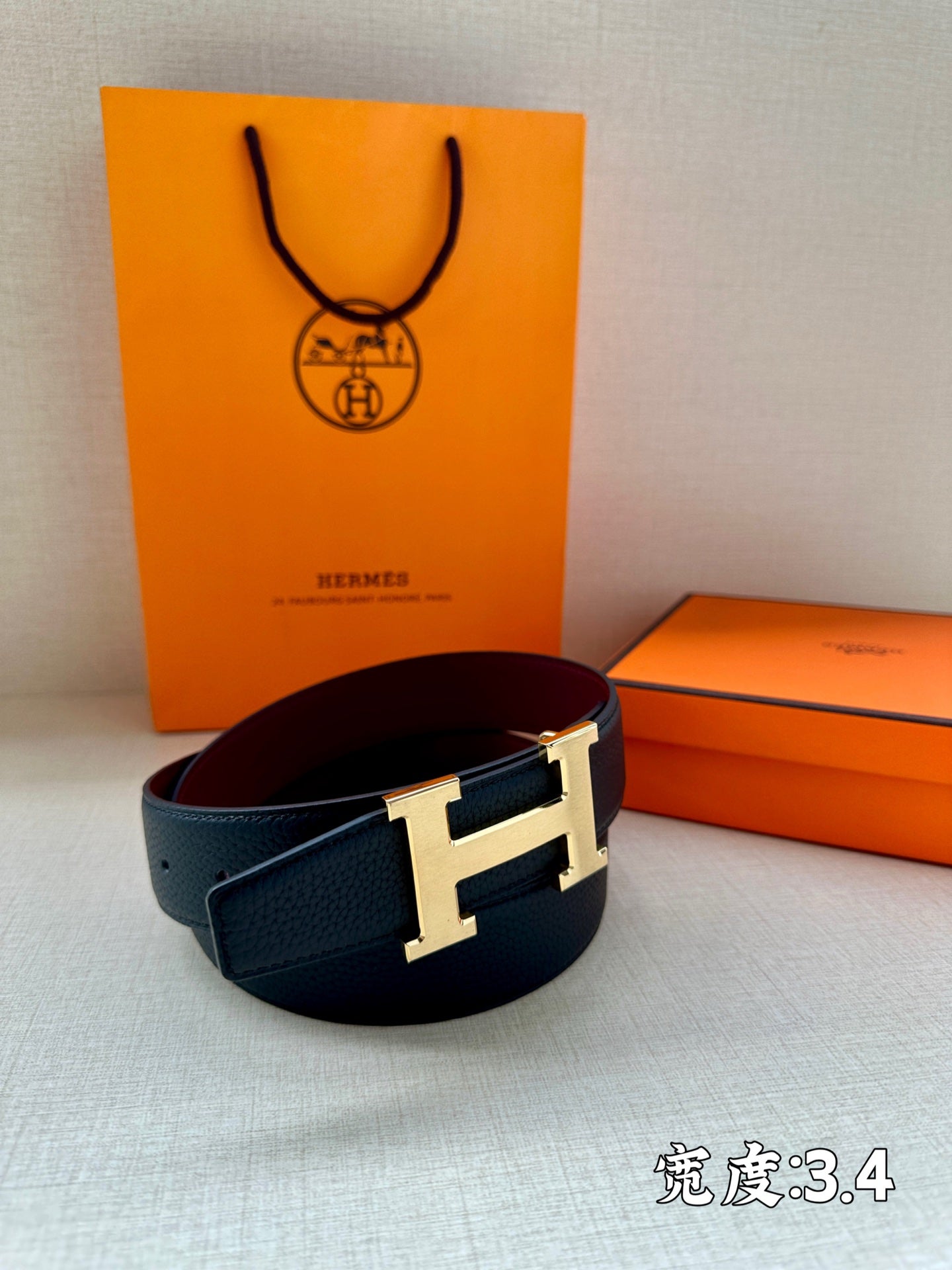 Navy leather belt with silver H buckle on orange box.