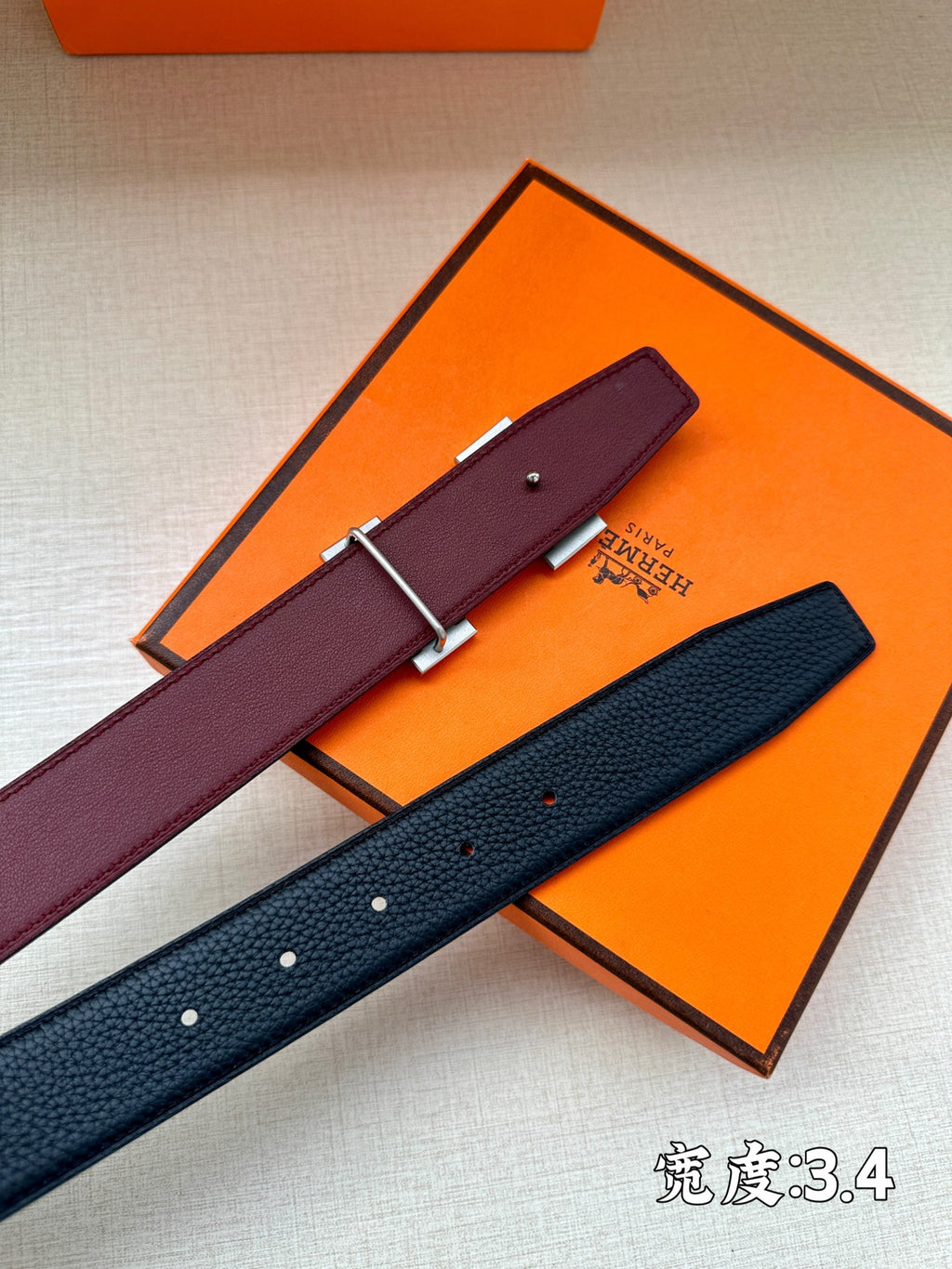 Burgundy and navy leather belts with silver H buckles in orange box.