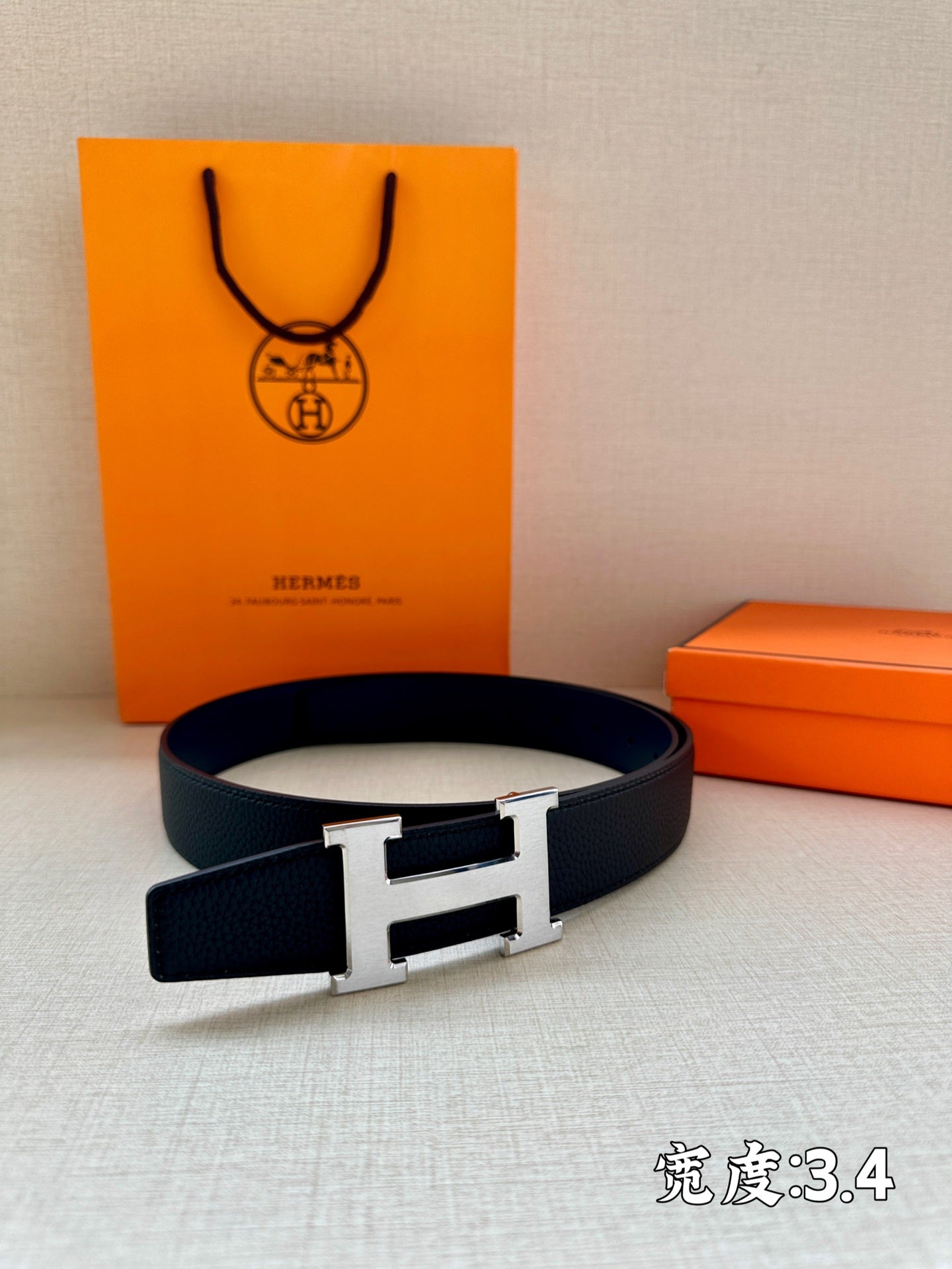 Hermes H-buckle belt in dark navy leather with gold-tone buckle, flat lay
