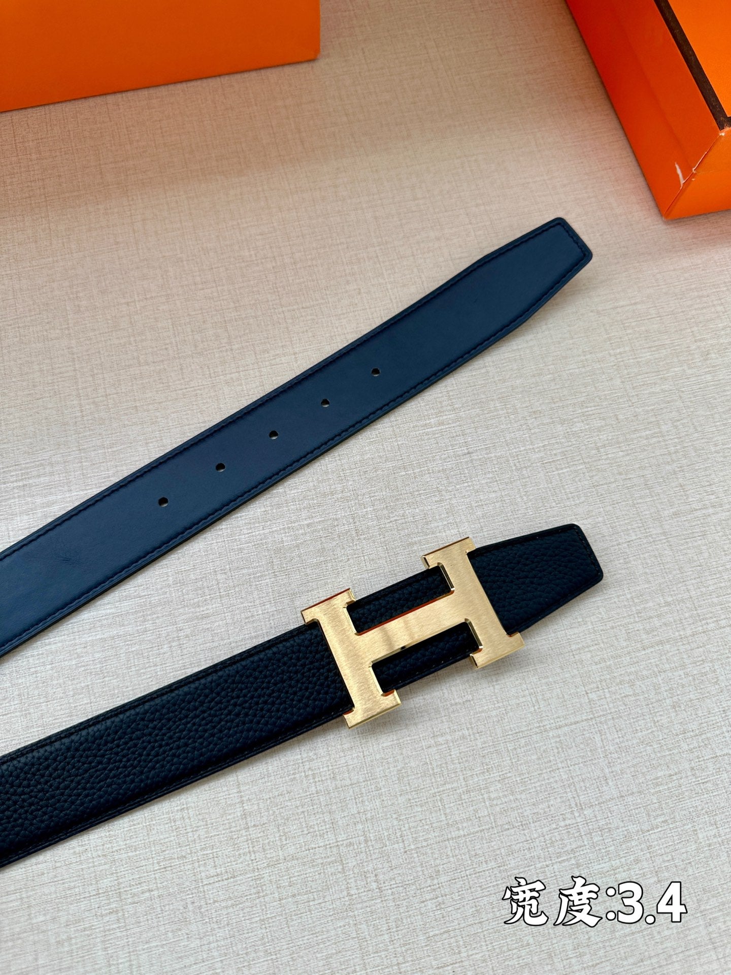 Hermes belt with dark navy leather strap and gold-tone H buckle on tabletop