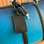 Gucci bag blue GG pattern with black leather luggage tag and gold hardware.