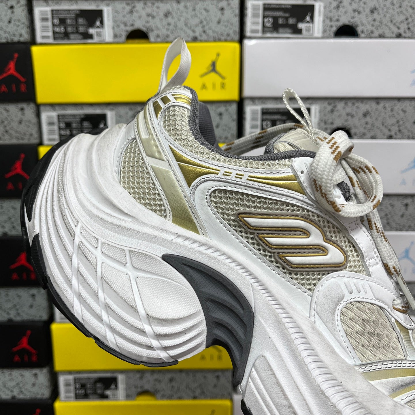 White Balenciaga sneakers with gold logo panel and white laces, chunky sole tread.