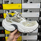 White Balenciaga sneakers with gold accents, mesh panels, chunky rubber sole, lace-up.