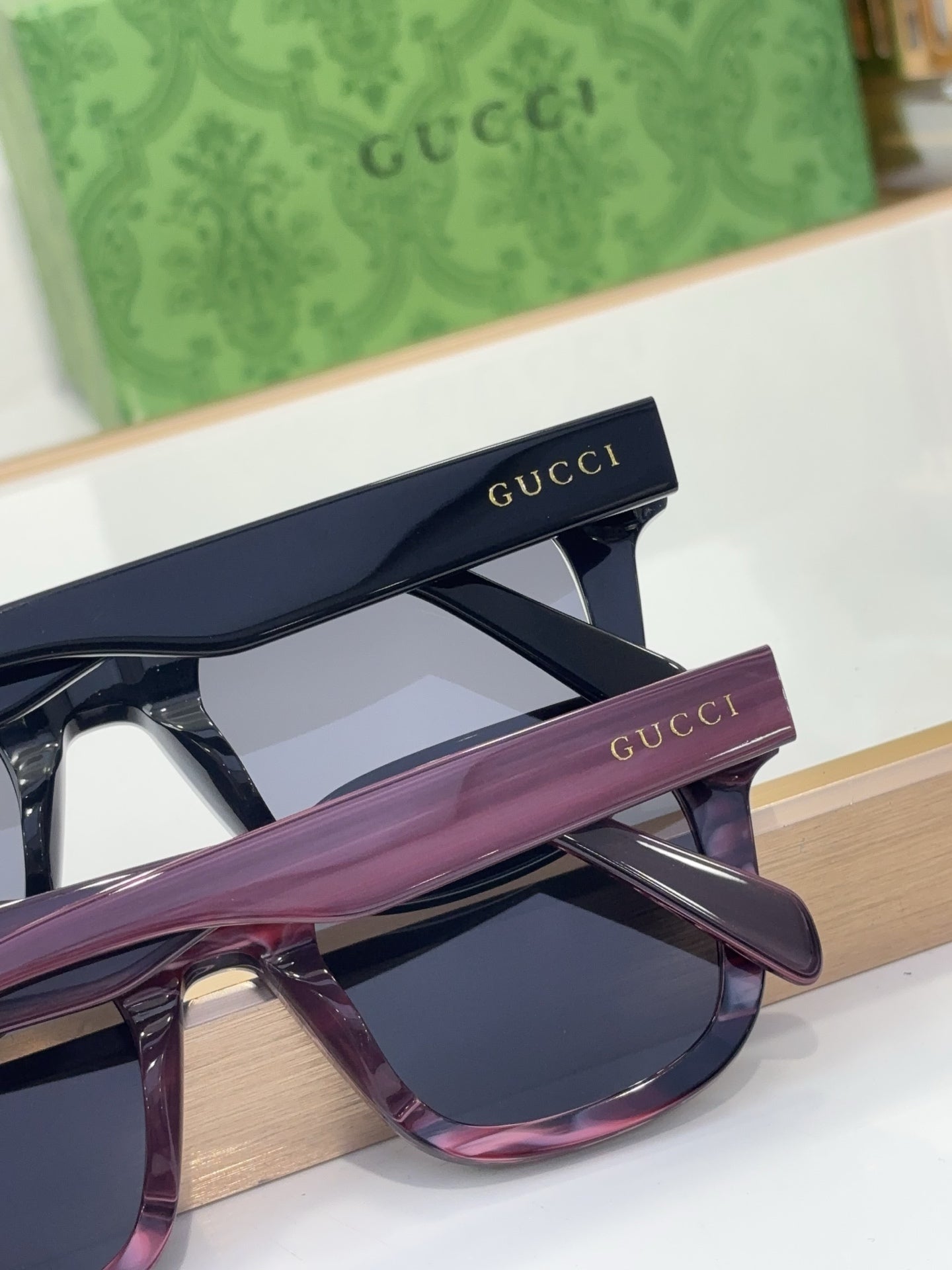 Gucci close-up of two sunglasses, navy and purple frames with branded temples