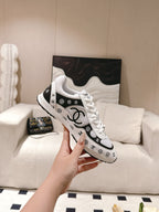 White Chanel sneakers with black logo pattern, held in hand
