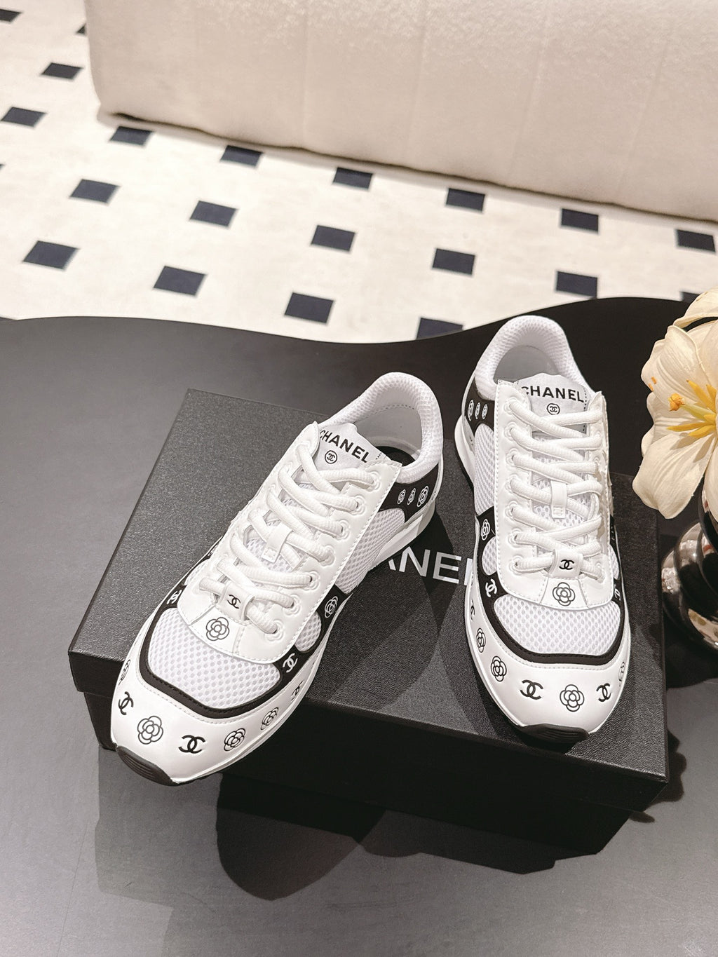 White low-top sneakers with white laces and black Chanel logo accents on sides