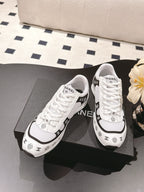 White low-top sneakers with white laces and black Chanel logo accents on sides