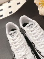 Two white Chanel sneakers showing laced uppers and black logo trim