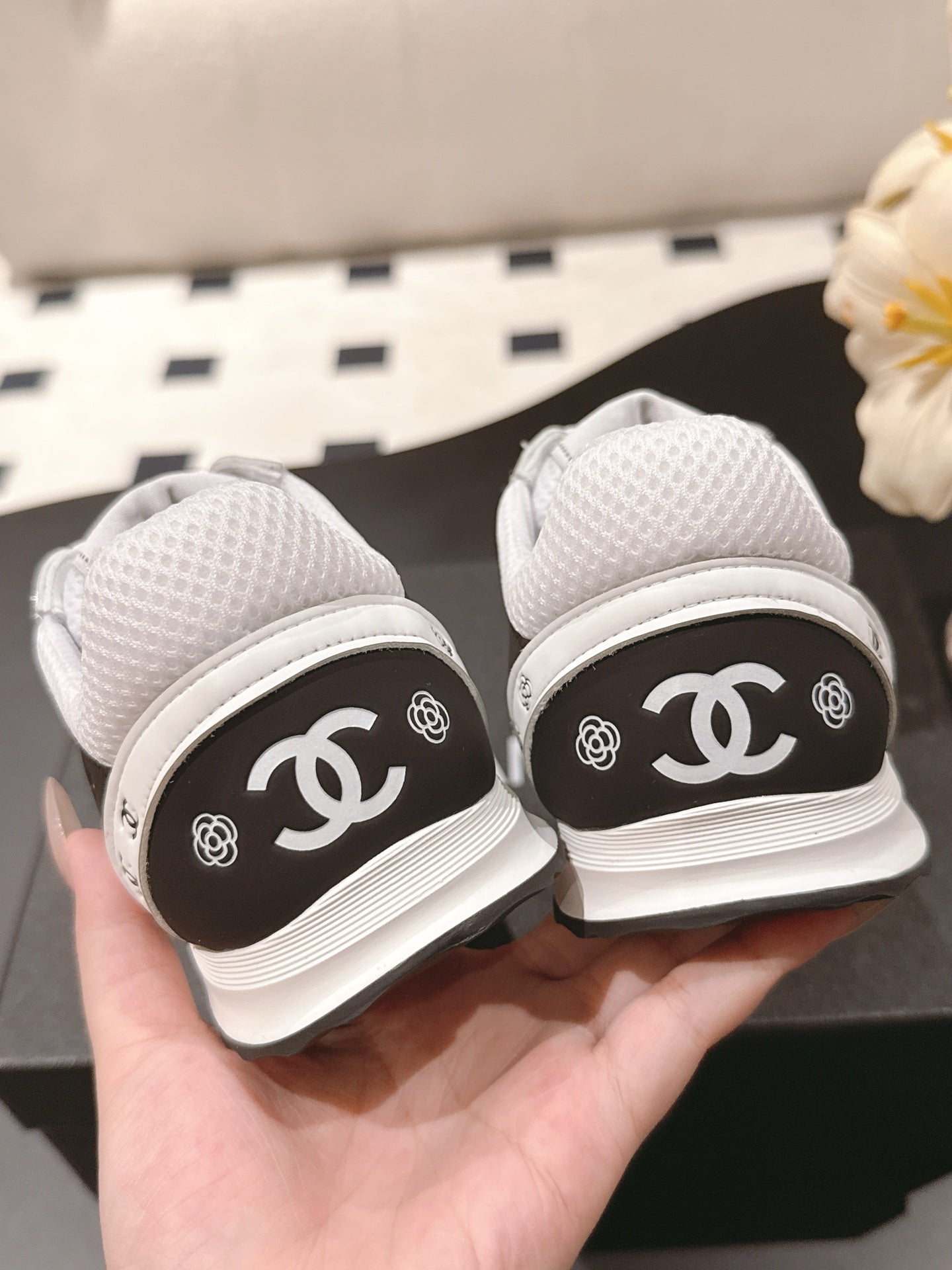 White low-top sneakers with black heel panels showing Chanel CC logos, back view