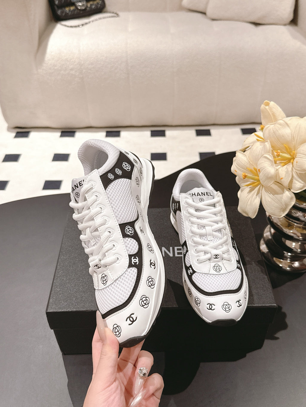 White low-top sneakers with black trim and Chanel CC logos, held in hand