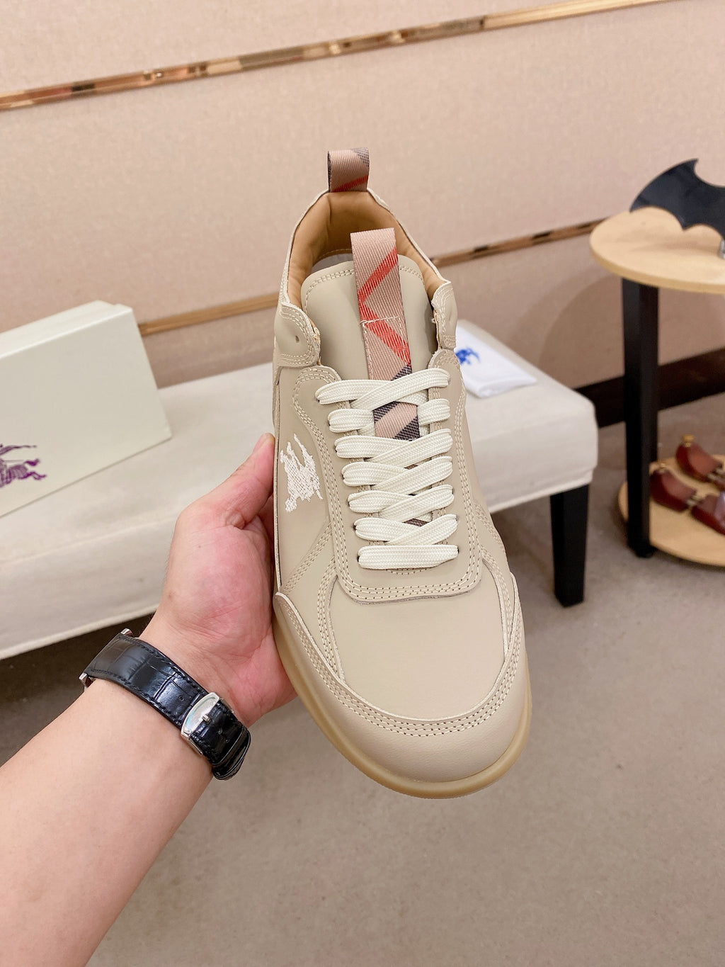 Cream lace-up sneaker held in hand, side logo panel and padded collar