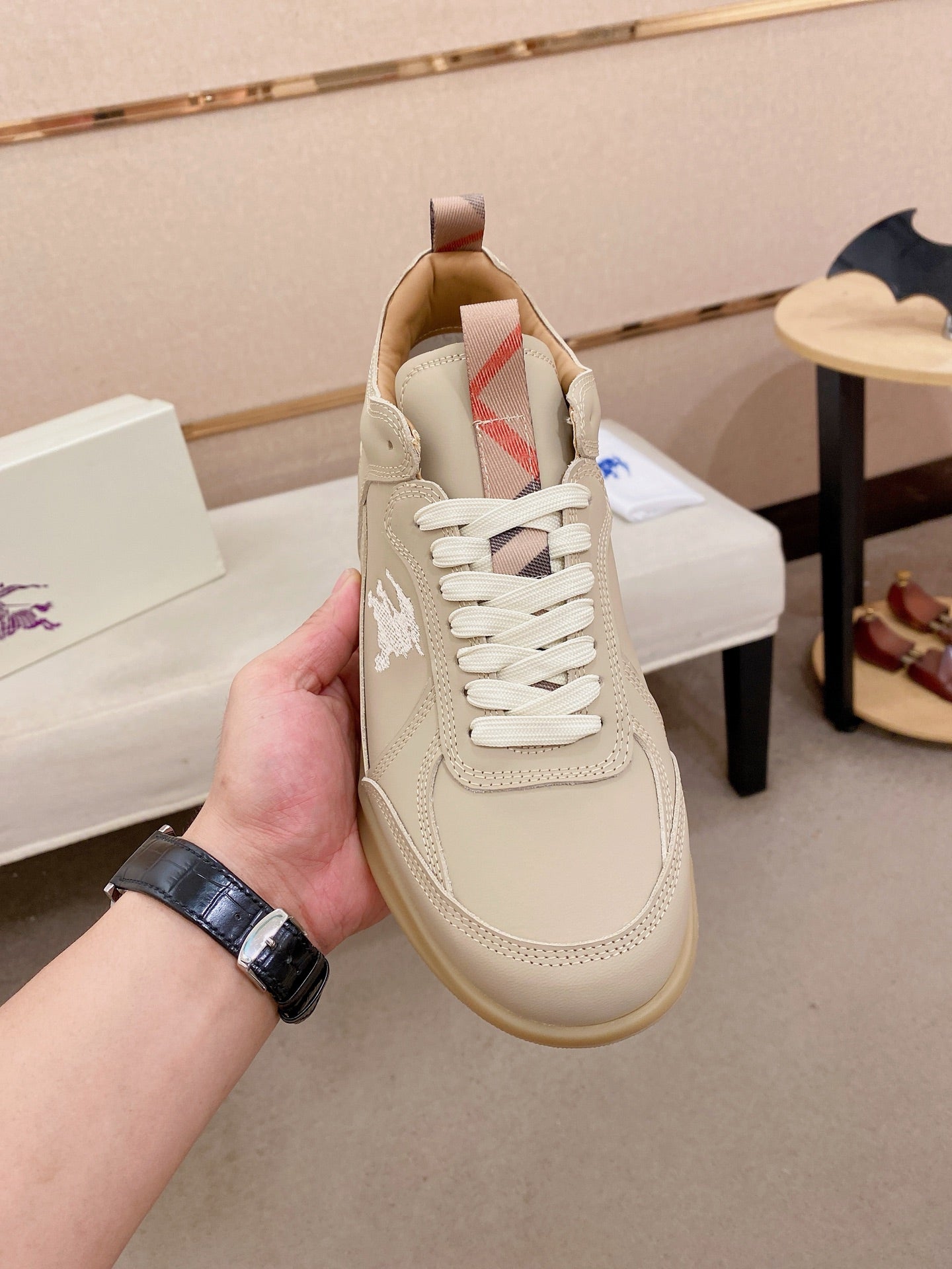 Cream lace-up sneaker held in hand, side logo panel and padded collar