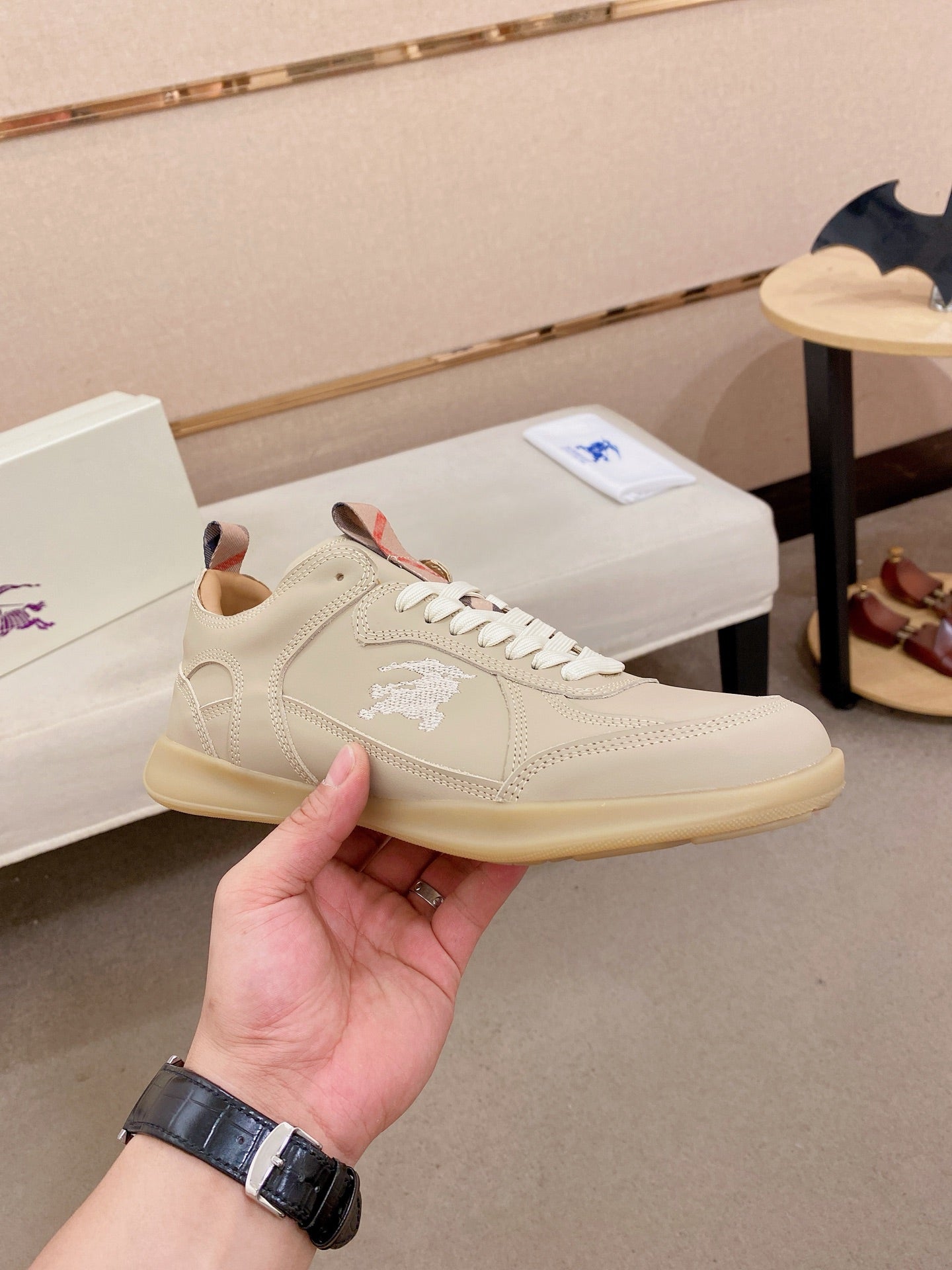 Cream low-top sneaker with lace-up closure, stitched logo and tan rubber sole