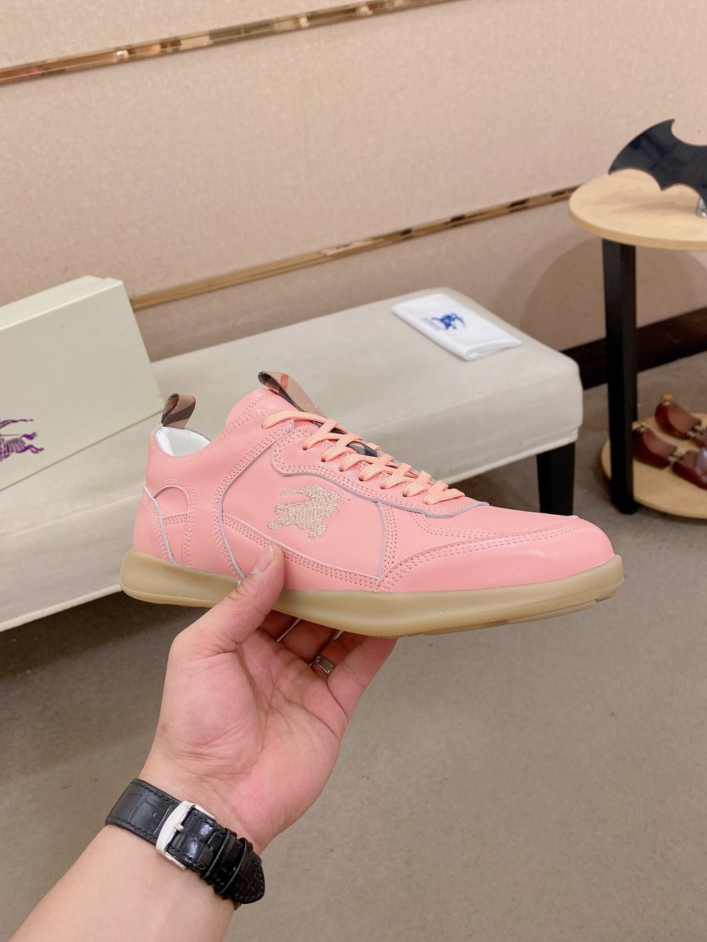 Burberry pink lace-up sneaker held in hand, side logo and cream sole visible