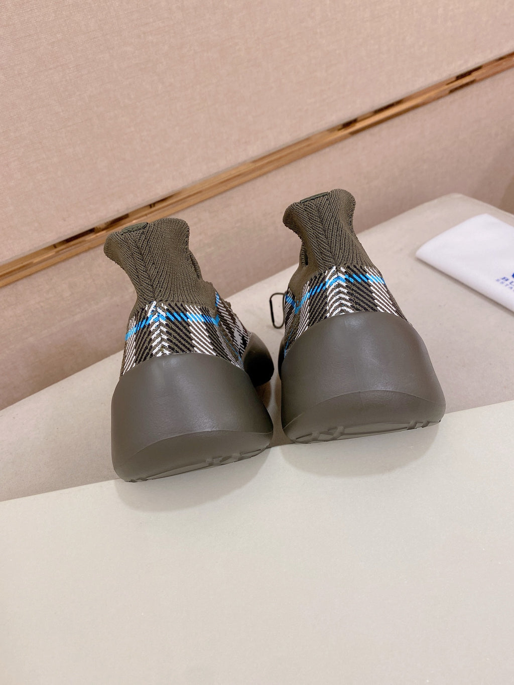 Gray knit sneakers showing heels with black-and-white plaid stripe and blue accents