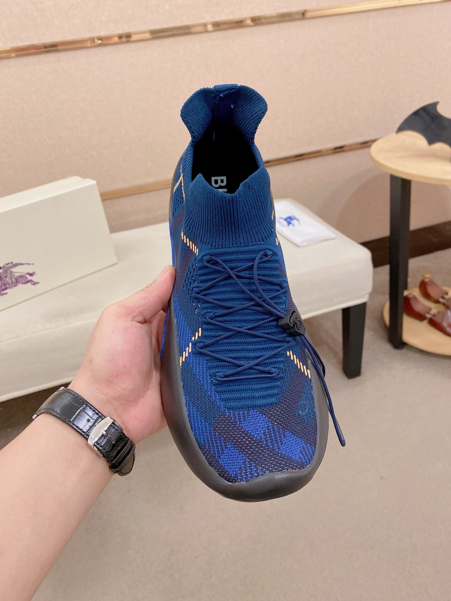 Blue knit sneaker held by hand, sock collar and lace-up front