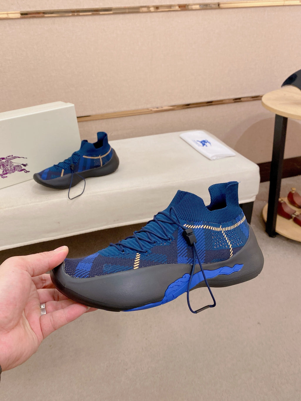 Blue knit sneaker with black sole, front side view on shoe box