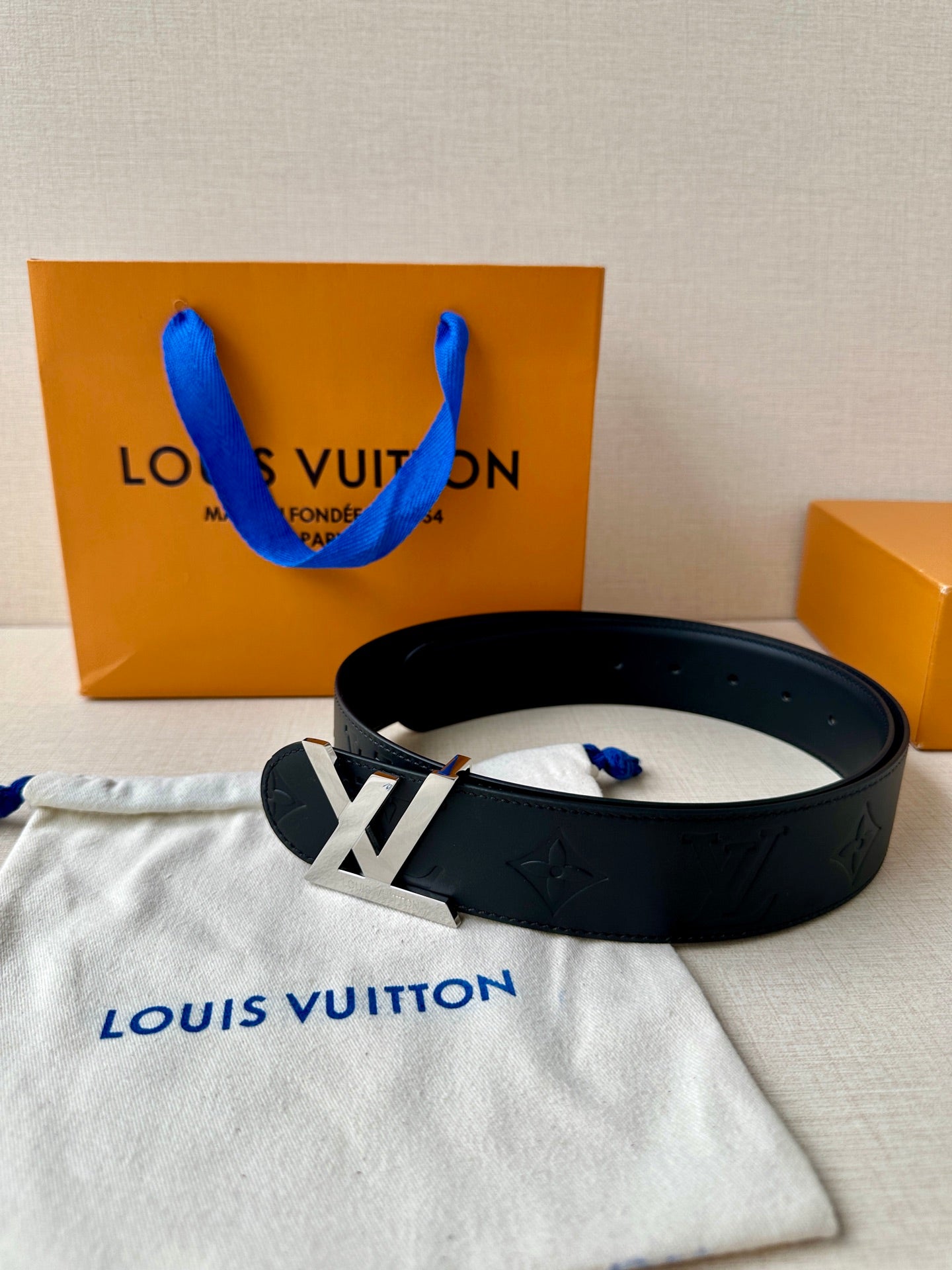 Black Louis Vuitton belt laid flat with gold-toned LV buckle and embossed pattern.