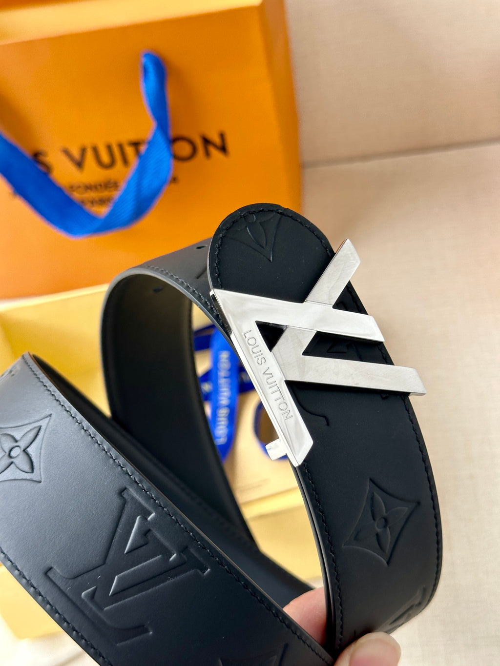 Black Louis Vuitton belt buckle close-up with LV motif on embossed leather strap.