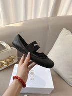 Black women's ballet flat with crisscross strap and logo patch, held in hand.