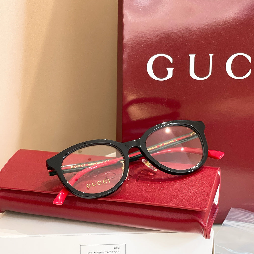 Gucci black round eyeglasses with red temple accents and Gucci logo.