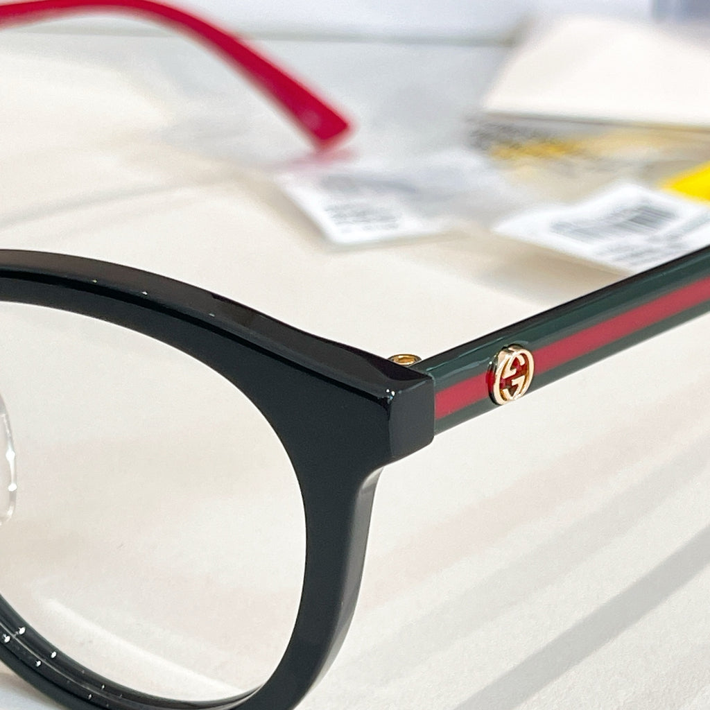 Gucci black eyeglass frame corner with green-and-red stripe and gold emblem.