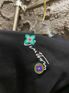 Black T-shirt embroidery detail with green flower and crest patches